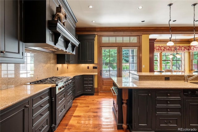 kitchen with stainless steel gas stovetop, light stone counters, backsplash, light wood-type flooring, and decorative light fixtures
