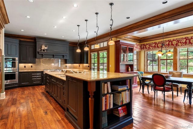 kitchen featuring double oven, open shelves, backsplash, light stone countertops, and a center island with sink
