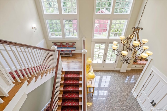 stairway featuring granite finish floor, a towering ceiling, a notable chandelier, and french doors