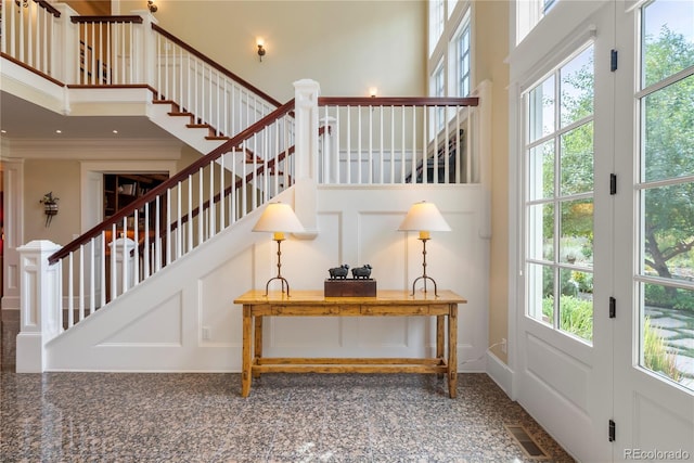 stairway with ornamental molding, a healthy amount of sunlight, a towering ceiling, and visible vents