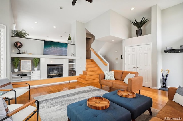 living area with stairs, recessed lighting, a tile fireplace, wood finished floors, and a ceiling fan