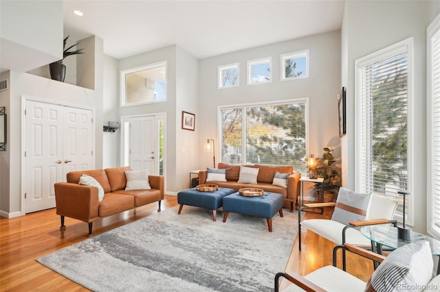 living room featuring recessed lighting, baseboards, light wood-style flooring, and a towering ceiling