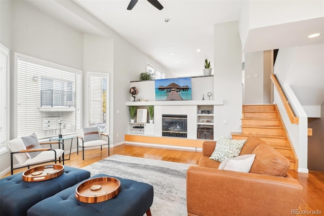 living room featuring a glass covered fireplace, baseboards, wood finished floors, and stairs