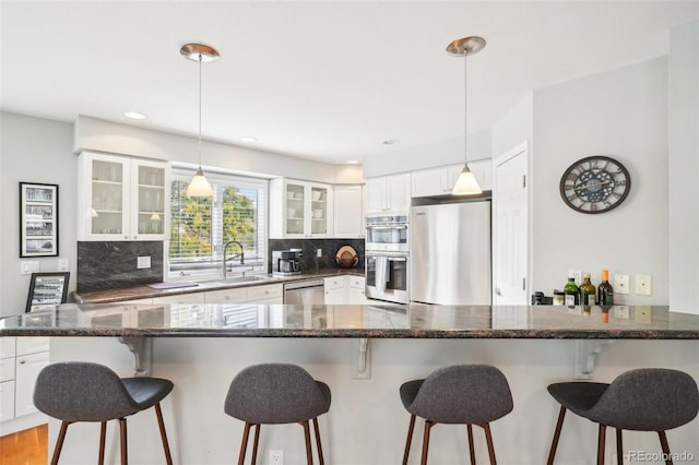 kitchen featuring tasteful backsplash, glass insert cabinets, a peninsula, stainless steel appliances, and a sink