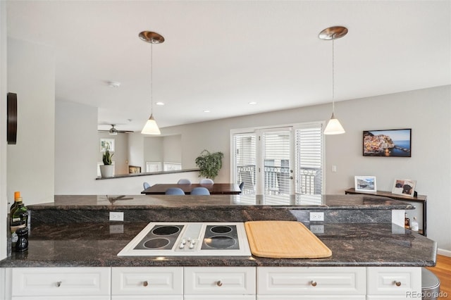 kitchen with white electric stovetop, dark stone counters, recessed lighting, hanging light fixtures, and white cabinetry