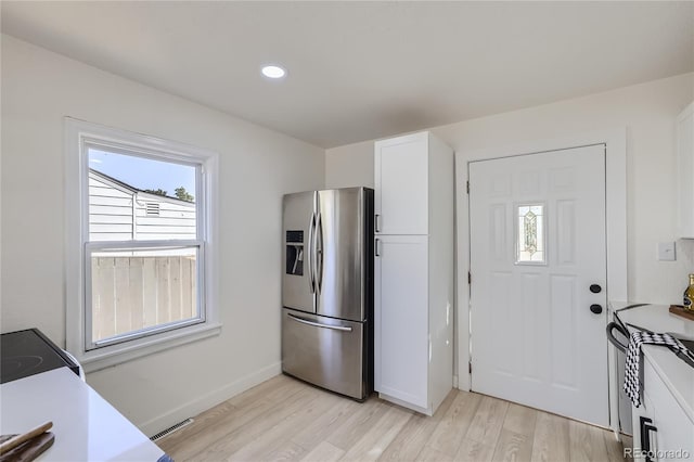 kitchen with stove, white cabinets, stainless steel refrigerator with ice dispenser, and light wood-type flooring