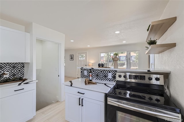 kitchen featuring white cabinets, stainless steel electric range, light wood-type flooring, and backsplash