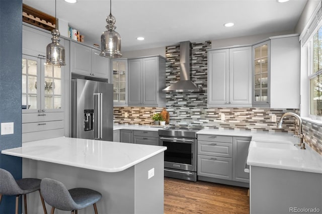 kitchen with a breakfast bar area, a sink, stainless steel appliances, gray cabinets, and wall chimney range hood