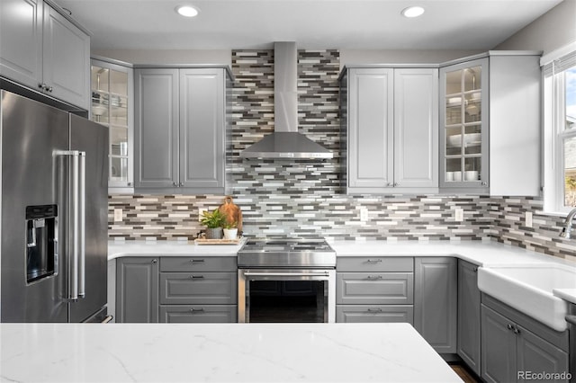 kitchen featuring wall chimney range hood, a sink, appliances with stainless steel finishes, and gray cabinets