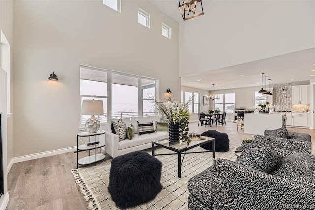 living room featuring an inviting chandelier, light hardwood / wood-style flooring, and a high ceiling