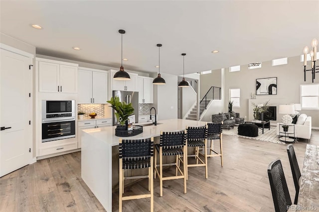 kitchen with pendant lighting, a breakfast bar area, appliances with stainless steel finishes, a kitchen island with sink, and white cabinets