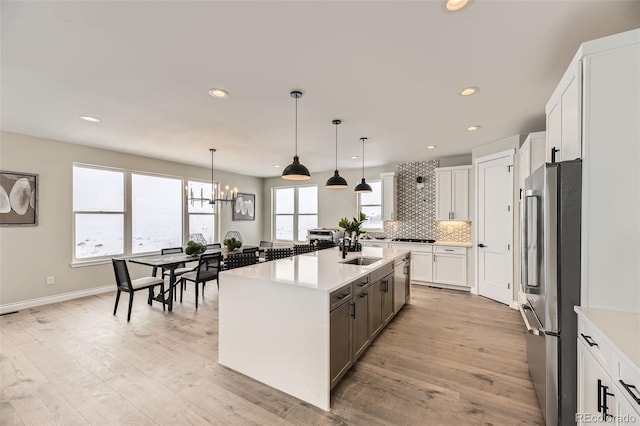 kitchen featuring sink, white cabinetry, decorative light fixtures, appliances with stainless steel finishes, and a kitchen island with sink