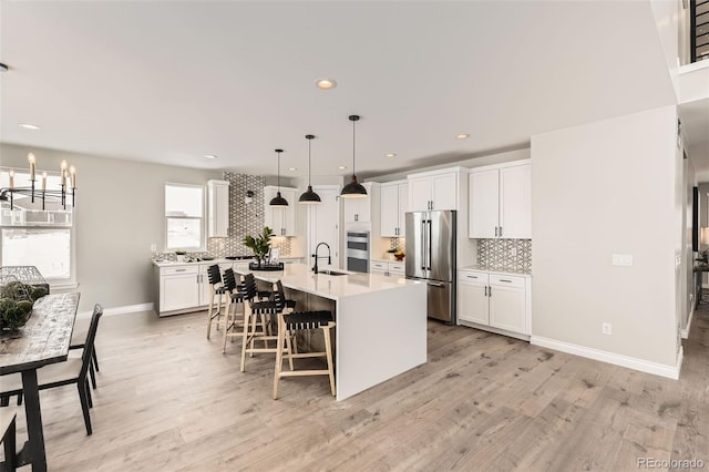 kitchen featuring pendant lighting, sink, white cabinets, stainless steel appliances, and a center island with sink