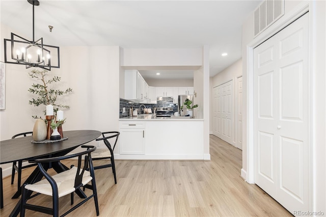 dining area featuring sink, light hardwood / wood-style floors, and an inviting chandelier