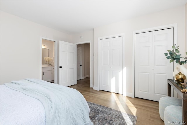 bedroom featuring connected bathroom, two closets, and light hardwood / wood-style flooring