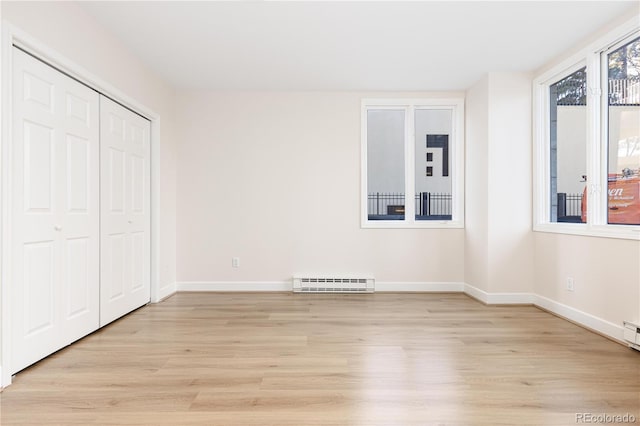 unfurnished bedroom with light wood-type flooring, a baseboard radiator, and a closet