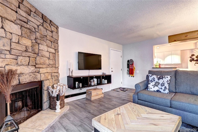 living room featuring a stone fireplace, hardwood / wood-style flooring, and a textured ceiling