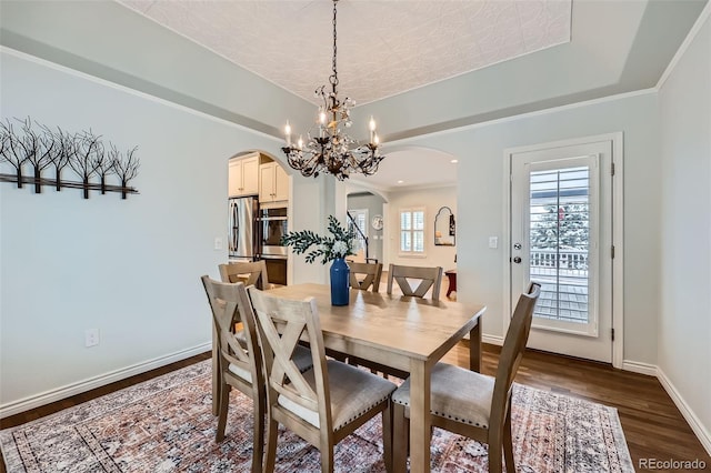 dining room with arched walkways, dark wood-style floors, a tray ceiling, and baseboards