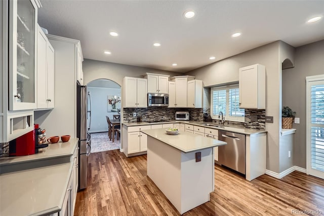 kitchen featuring light wood-type flooring, white cabinetry, arched walkways, appliances with stainless steel finishes, and decorative backsplash