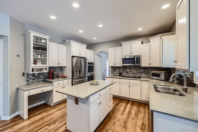 kitchen with light wood finished floors, a sink, arched walkways, appliances with stainless steel finishes, and a toaster