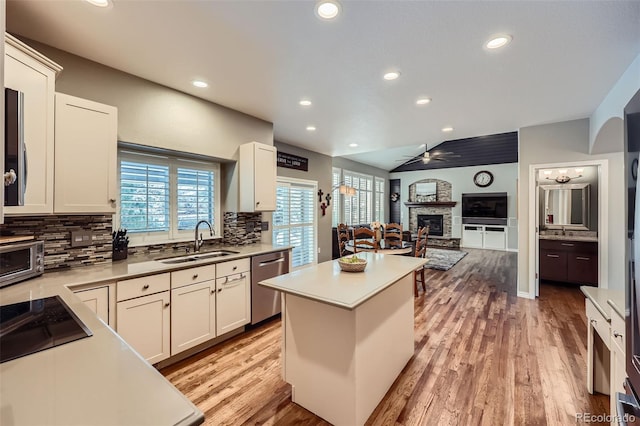 kitchen with light wood finished floors, a sink, a stone fireplace, dishwasher, and black electric cooktop