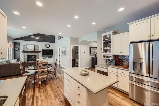 kitchen featuring a ceiling fan, stainless steel refrigerator with ice dispenser, arched walkways, a stone fireplace, and light countertops