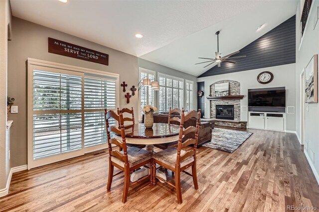 dining space with a ceiling fan, vaulted ceiling, wood finished floors, and a fireplace