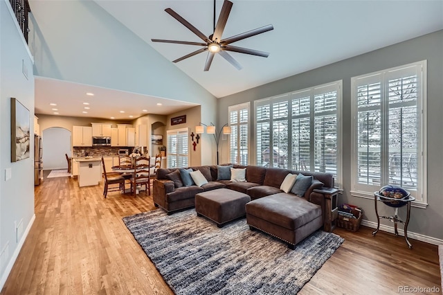 living room with arched walkways, light wood finished floors, high vaulted ceiling, and baseboards