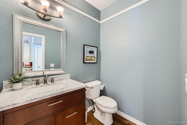 half bathroom featuring baseboards, toilet, wood finished floors, a textured wall, and vanity