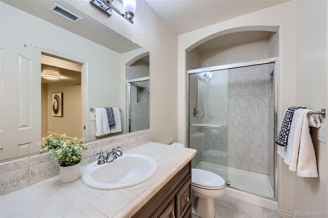 full bathroom with vanity, a shower stall, toilet, and visible vents