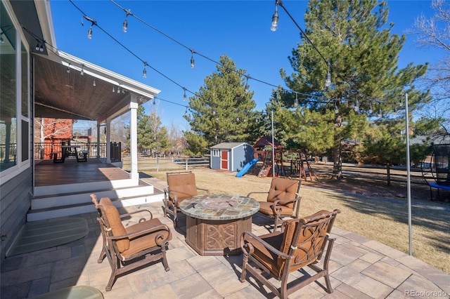 view of patio featuring fence, a shed, an outdoor fire pit, an outdoor structure, and a playground