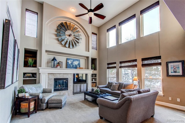 living room with a towering ceiling, a tile fireplace, ceiling fan, and light carpet