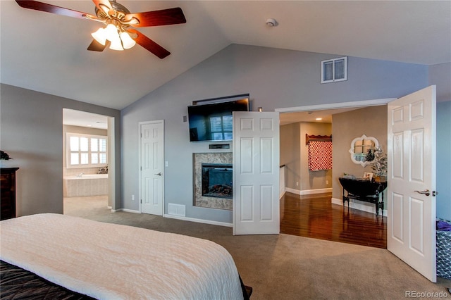 bedroom with ensuite bath, vaulted ceiling, carpet floors, a tiled fireplace, and ceiling fan