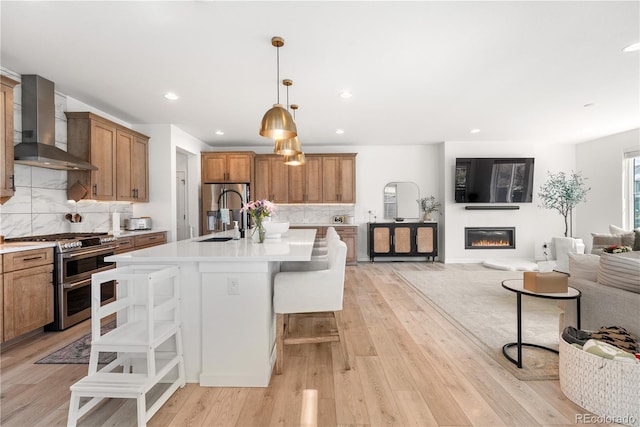 9140 Moondance Dr, Littleton, CO 80125 - kitchen featuring wall chimney range hood, appliances with stainless steel finishes, a sink, open floor plan, and brown cabinetry