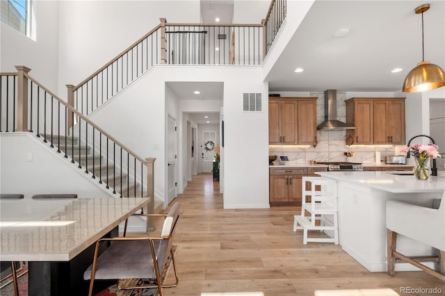 9140 Moondance Dr, Littleton, CO 80125 - kitchen with wall chimney exhaust hood, a high ceiling, brown cabinets, light wood-type flooring, and a kitchen breakfast bar