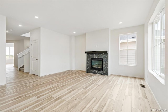 unfurnished living room with light hardwood / wood-style flooring, a high end fireplace, and a healthy amount of sunlight