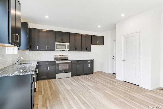 kitchen featuring light wood-type flooring, stainless steel appliances, light stone counters, and sink