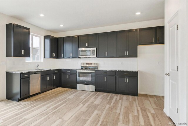 kitchen with light stone countertops, appliances with stainless steel finishes, light hardwood / wood-style floors, and decorative backsplash