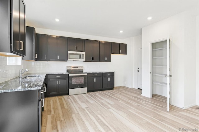 kitchen with light stone countertops, appliances with stainless steel finishes, light wood-type flooring, and sink