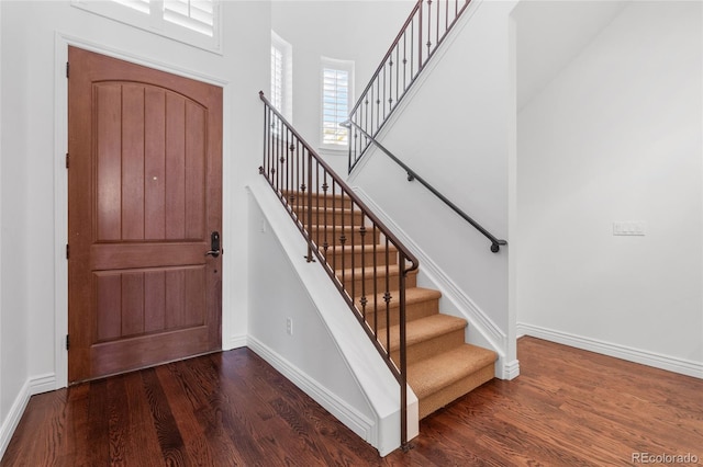 entrance foyer featuring dark wood-style floors, baseboards, stairway, and a high ceiling