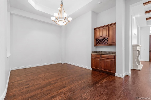 unfurnished dining area featuring a raised ceiling, dark wood-type flooring, and a notable chandelier