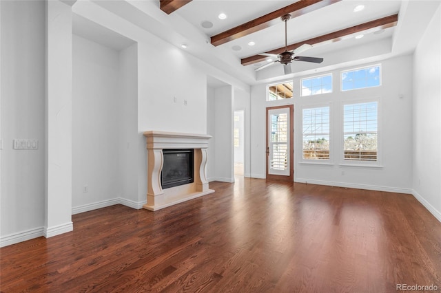 unfurnished living room featuring baseboards, beamed ceiling, dark wood-style flooring, and a glass covered fireplace