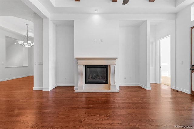 unfurnished living room featuring dark wood-type flooring, an inviting chandelier, a glass covered fireplace, and baseboards