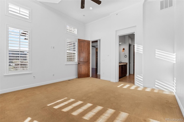 unfurnished bedroom with ensuite bath, light colored carpet, ornamental molding, ceiling fan, and a high ceiling