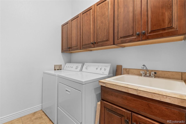 laundry area with cabinet space, light tile patterned floors, baseboards, washing machine and clothes dryer, and a sink