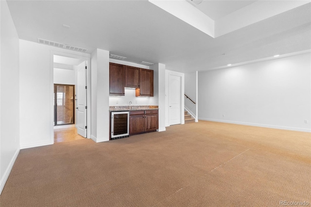 unfurnished living room featuring light colored carpet, beverage cooler, and wet bar