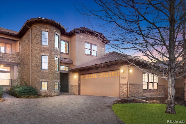 view of front of house featuring a garage, stone siding, a tiled roof, decorative driveway, and stucco siding