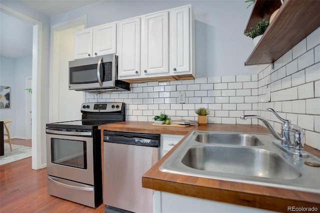 kitchen with appliances with stainless steel finishes, light wood-type flooring, tasteful backsplash, sink, and white cabinets