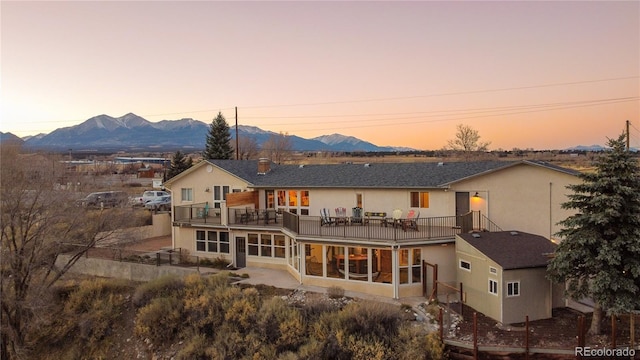 back house at dusk with a mountain view, a sunroom, and a balcony