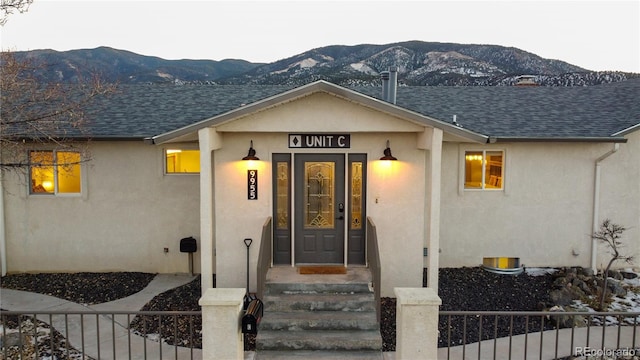 entrance to property featuring a shingled roof, a mountain view, and stucco siding